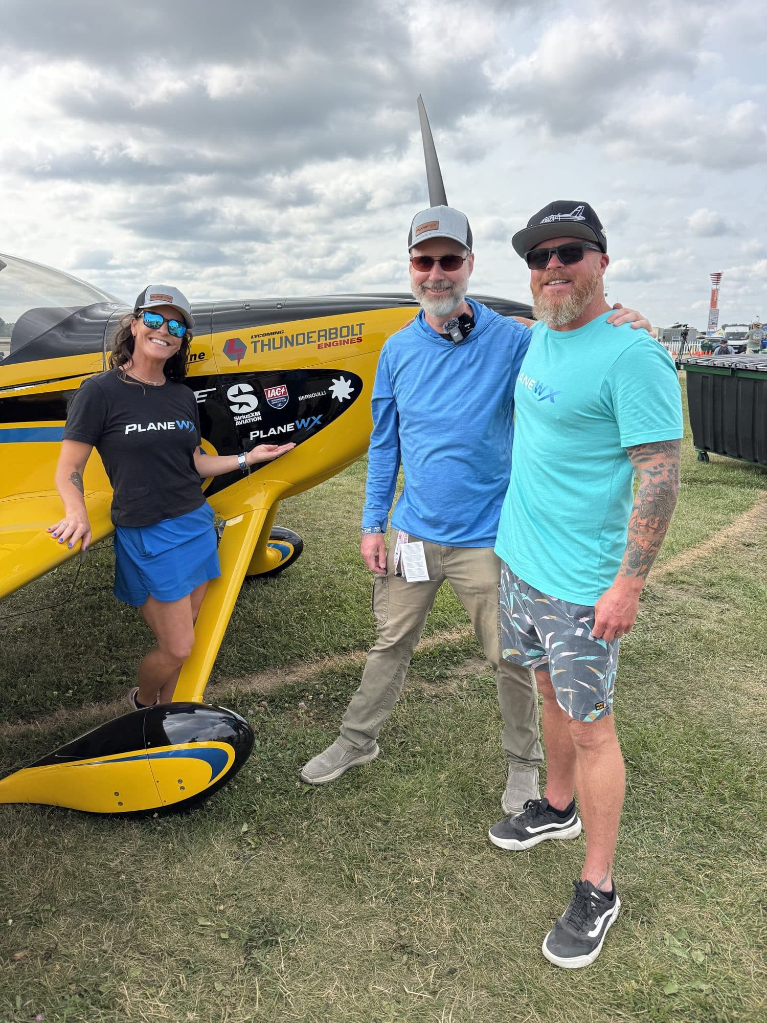 Sara Wolfgang, Flight Chops, and Mark Wolfgang beside the yellow RV-14 with PlaneWX logos at Oshkosh